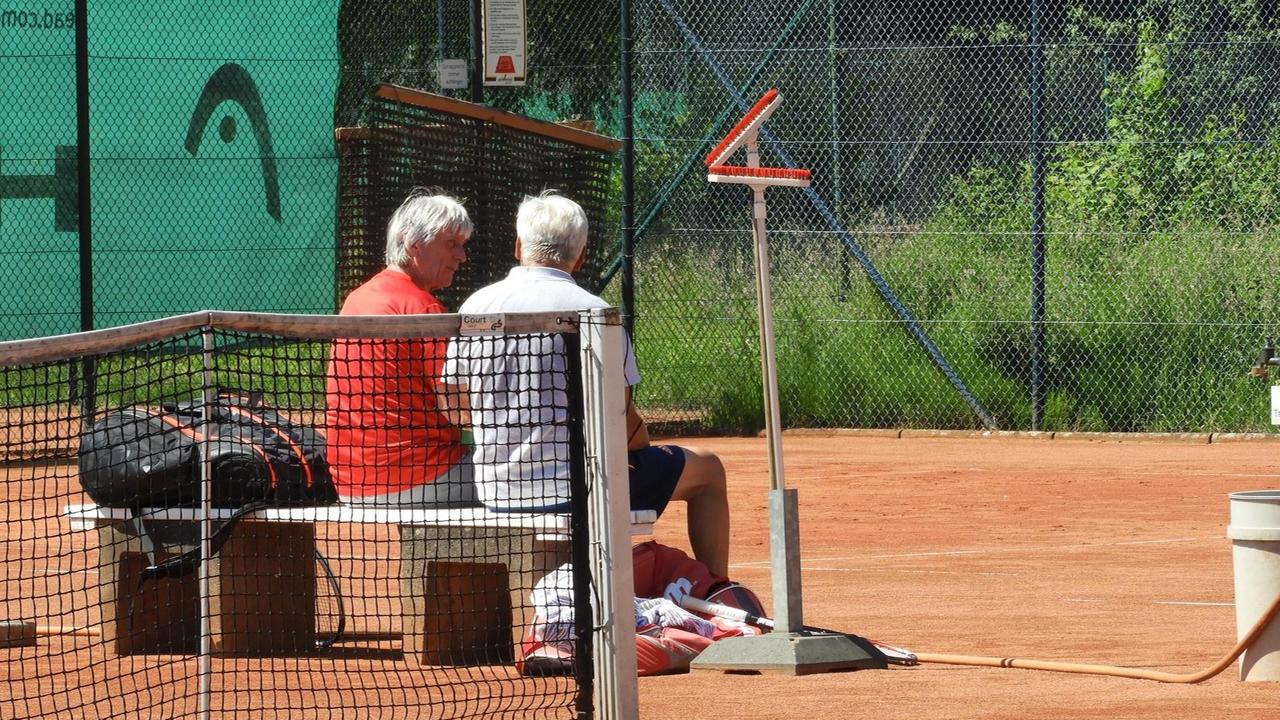 Zwei Tennisspieler ruhen sich auf einer Bank auf dem Tennisplatz aus Zwei Tennisspieler ruhen sich auf einer Bank auf dem Tennisplatz aus