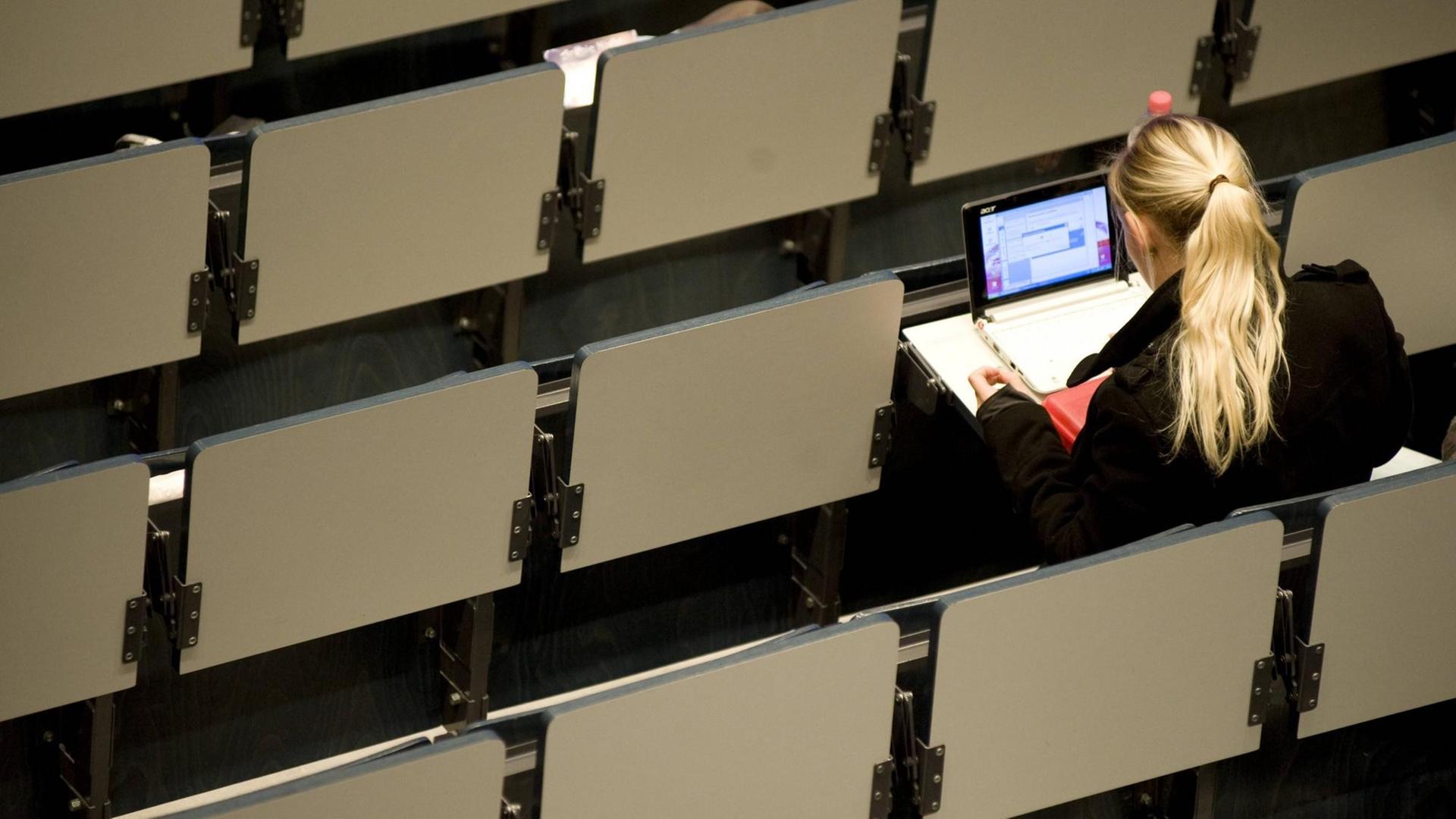 Eine Studentin sitzt allein in einem Hörsaal am Laptop Eine Studentin sitzt allein in einem Hörsaal am Laptop