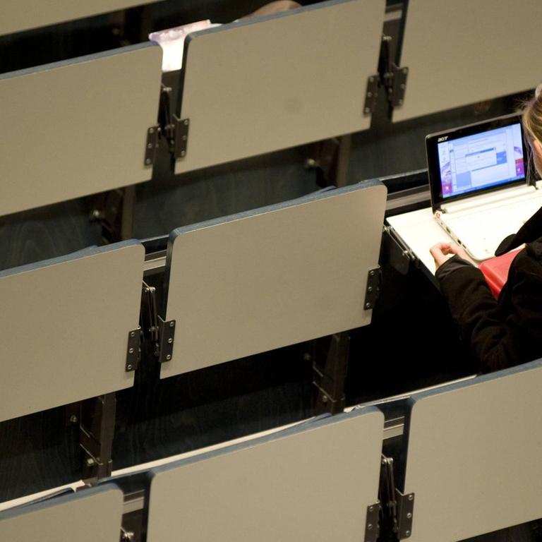 Eine Studentin sitzt allein in einem Hörsaal am Laptop 