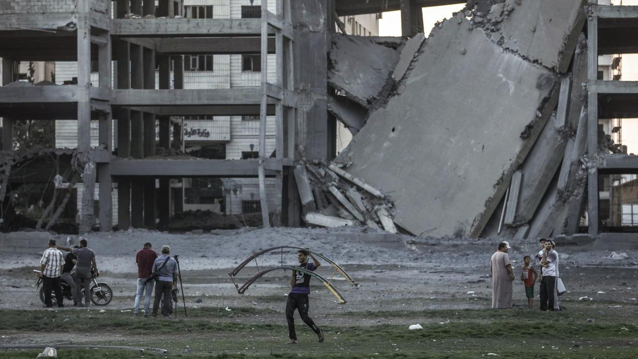 Ein Palästinenser trägt einen Metallrahmen neben einem zerbombten Gebäude. Ein Palästinenser trägt einen Metallrahmen neben einem zerbombten Gebäude.