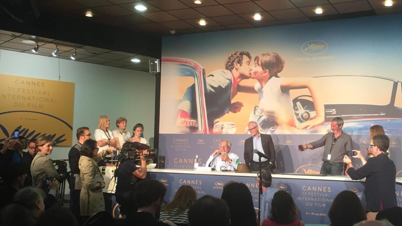 Foto von der Pressekonferenz mit Jean-Luc Godard, der per FaceTime zugeschalten war. Im Hintergrund ist das diesjährige Plakat der Filmfestspiele Cannes zu sehen, das eine Szene aus einem Godard-Film zeigt.