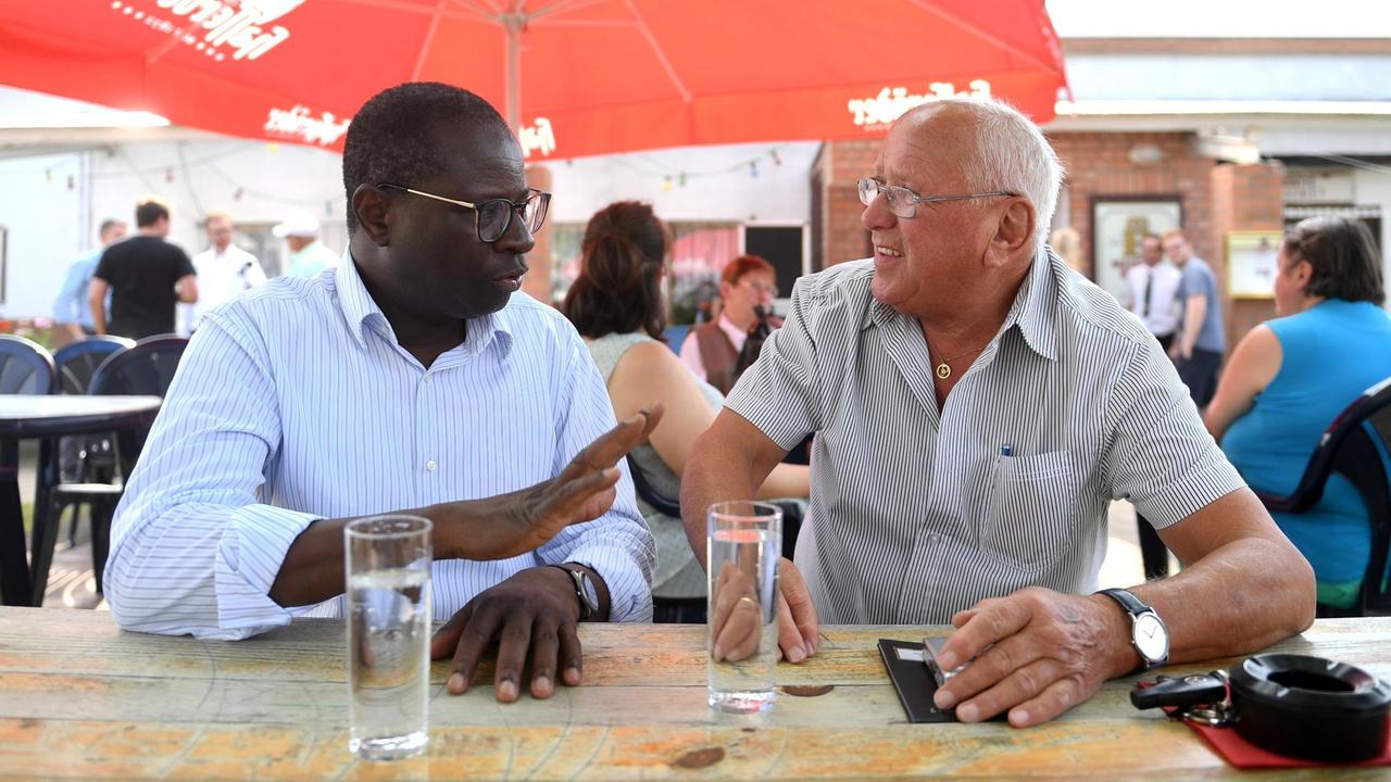 Der hallesche SPD Bundestagsabgeordnete Karamba Diaby (l.) unterhält sich am 08.08.2017 in der Kleingartenanlage «Am Pfarrberg» in Landsberg (Sachsen-Anhalt) mit dem Rentner Klaus Duschek. Diaby stammt aus dem Senegal, hat in Halle Chemie studiert und ist seit 2013 Mitglied des Deutschen Bundestages. Der hallesche SPD Bundestagsabgeordnete Karamba Diaby (l.) unterhält sich am 08.08.2017 in der Kleingartenanlage «Am Pfarrberg» in Landsberg (Sachsen-Anhalt) mit dem Rentner Klaus Duschek. Diaby stammt aus dem Senegal, hat in Halle Chemie studiert und ist seit 2013 Mitglied des Deutschen Bundestages.