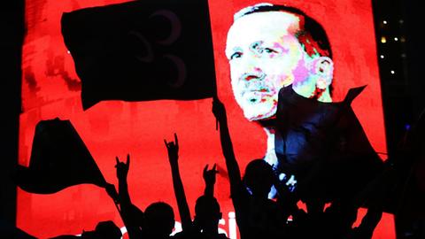 Erdogan-Anhänger mit Fahnen, im Hintergrund Porträt von Erdogan auf einem Bildschirm