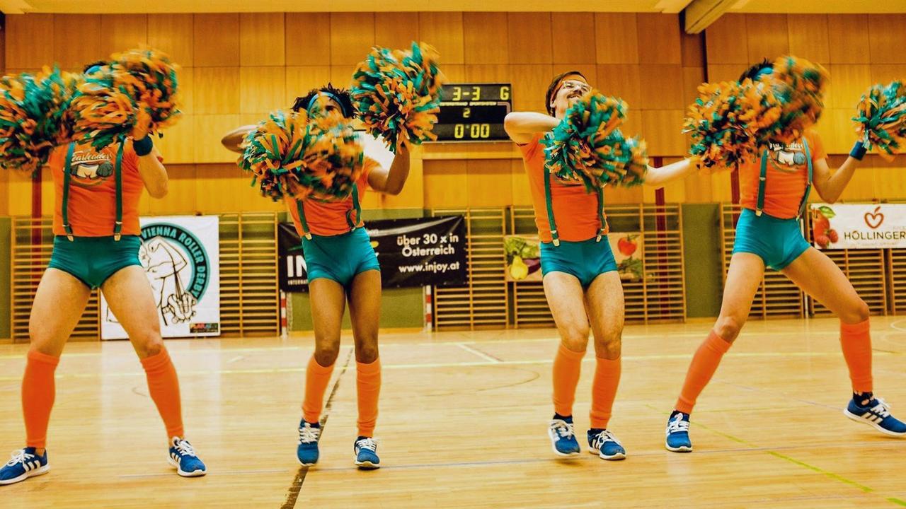 Vier Mitglieder der Vienna Fearleaders tanzen in engen türkisen Höschen und mit Pompons in einer Sporthalle. Vier Mitglieder der Vienna Fearleaders tanzen in engen türkisen Höschen und mit Pompons in einer Sporthalle.