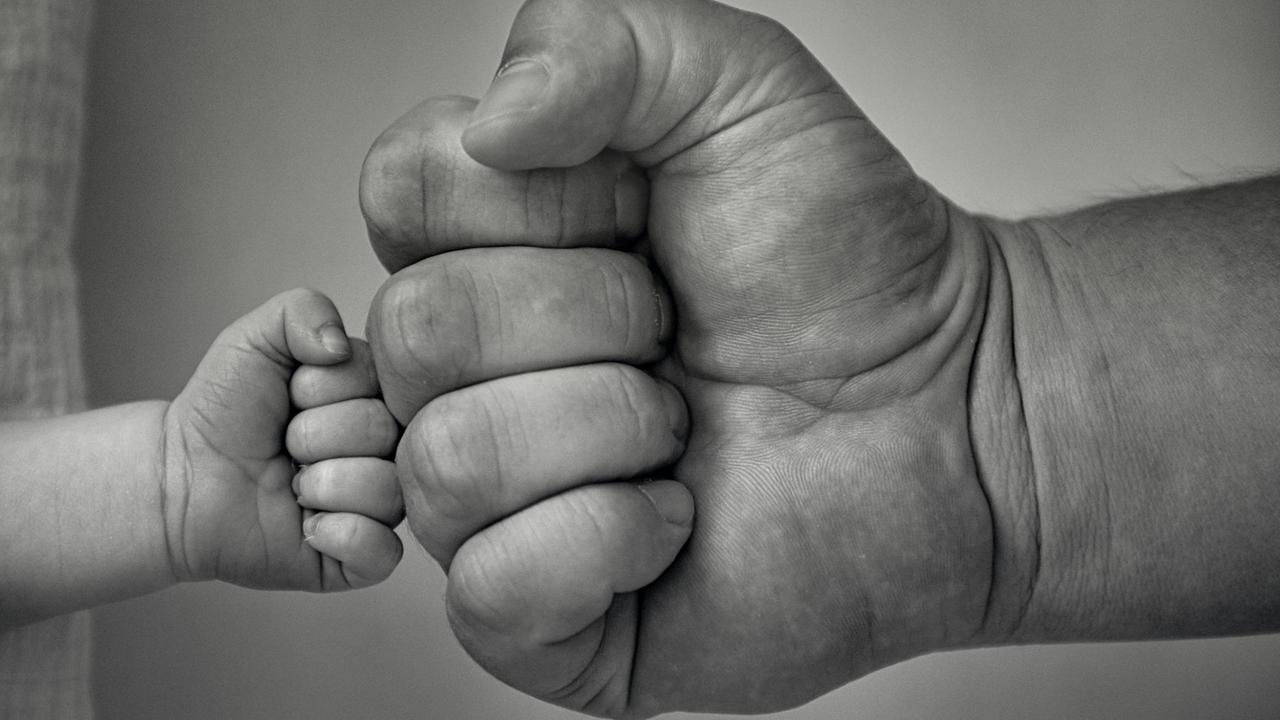 Schwarz-weiß-Fotografie einer Kinder- und einer Männerhand, die zum Gruß zusammengeführt werden Schwarz-weiß-Fotografie einer Kinder- und einer Männerhand, die zum Gruß zusammengeführt werden