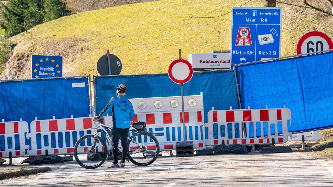 Ein Mann mit einem Mountainbike steht auf der deutschen Seite vor der mit einem Bauzaun und blauer Plane abgesperrten Grenze zwischen dem Aschauer Ortsteil Sachrang und Niederndorferberg im Kufsteinerland in Tirol. Ein Mann mit einem Mountainbike steht auf der deutschen Seite vor der mit einem Bauzaun und blauer Plane abgesperrten Grenze zwischen dem Aschauer Ortsteil Sachrang und Niederndorferberg im Kufsteinerland in Tirol.