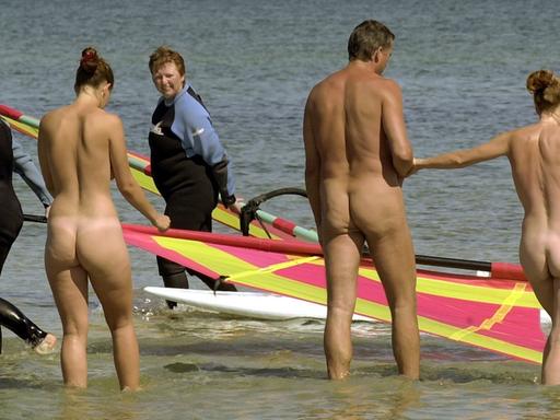 Nackte Schwimmer gehen am Ostseestrand ins Wasser. Zwei Surfer schauen ihnen zu.
