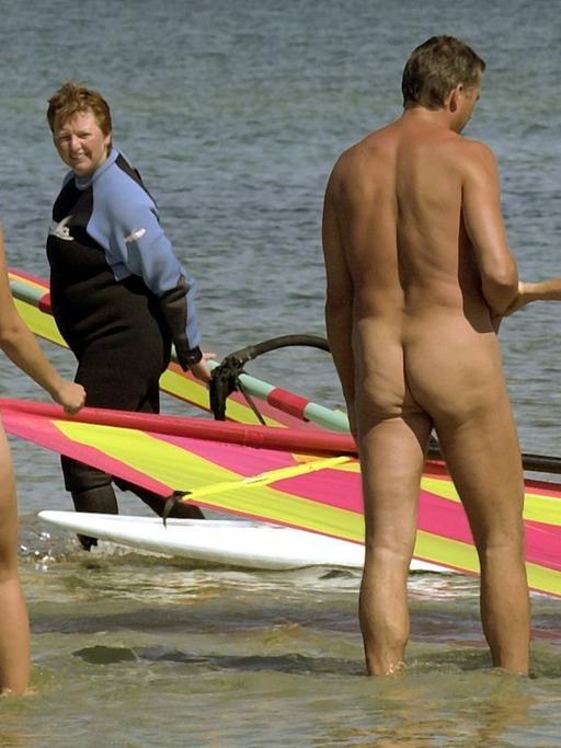 Nackte Schwimmer gehen am Ostseestrand ins Wasser. Zwei Surfer schauen ihnen zu.