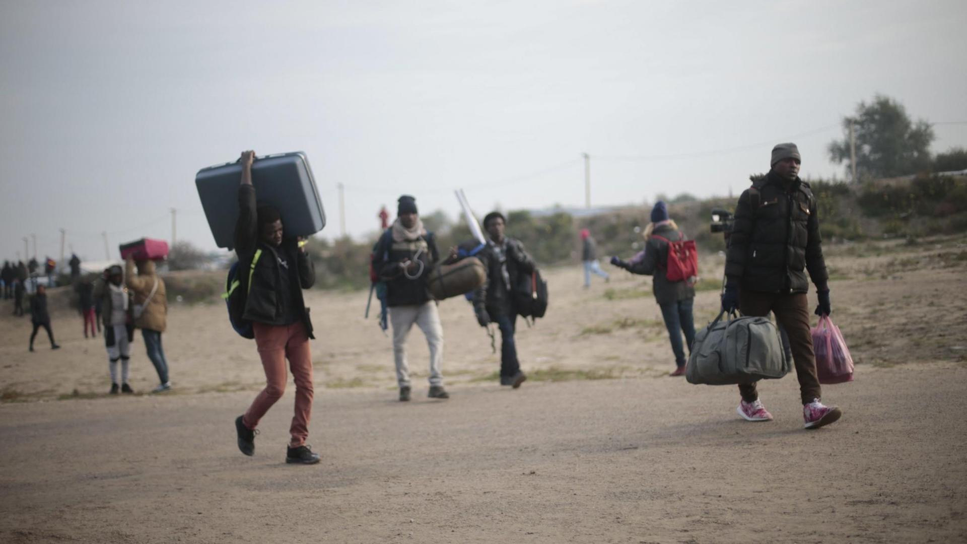 Migranten im Flüchtlingslager von Calais machen sich nach der begonnenen Räumung mit ihrem Gepäck auf den Weg. Migranten im Flüchtlingslager von Calais machen sich nach der begonnenen Räumung mit ihrem Gepäck auf den Weg.