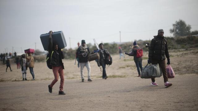 Migranten im Flüchtlingslager von Calais machen sich nach der begonnenen Räumung mit ihrem Gepäck auf den Weg.