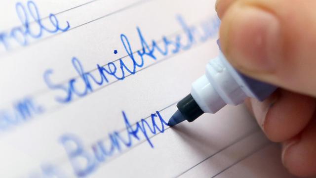 Ein Kind schreibt in Berlin mit verbundener Schreibschrift, der Schulausgangsschrift, in ein Schulheft.