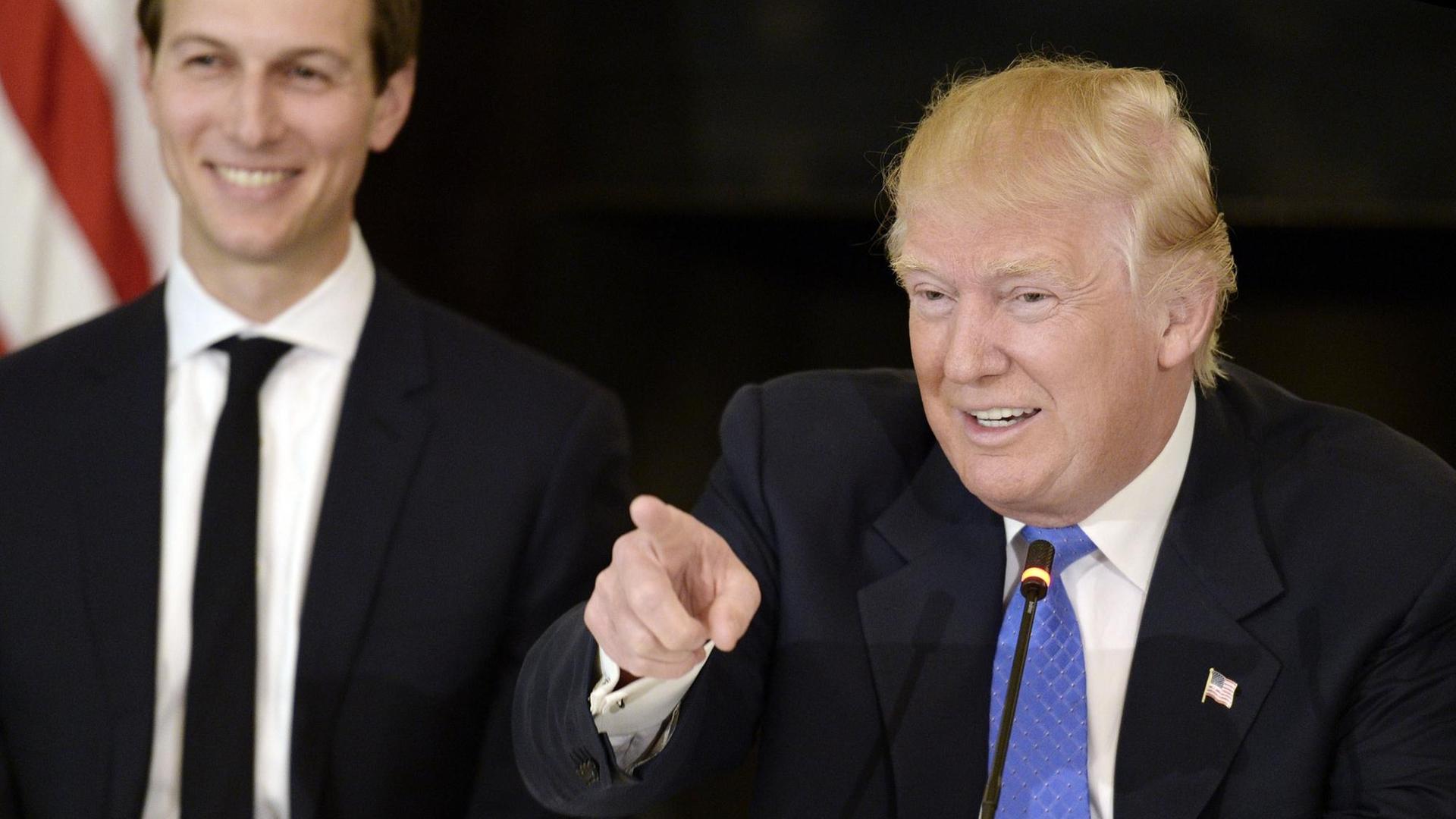 US-Präsident Donald Trump spricht und lacht dabei. Im Hintergrund ist sein Schwiegersohn Jared Kushner zu sehen.