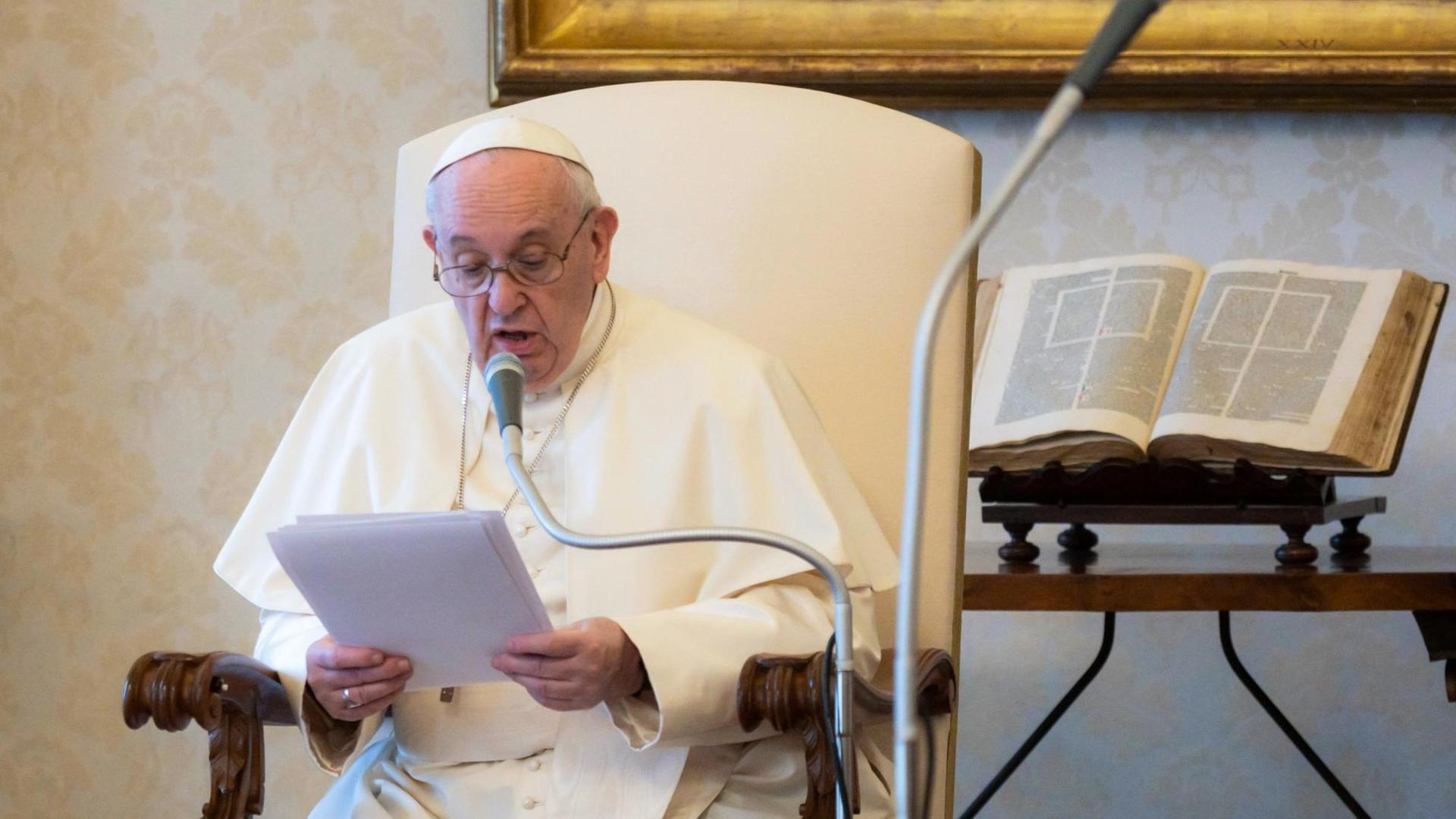 Papst Franziskus sitzt in einem Stuhl und liest etwas vor. Papst Franziskus sitzt in einem Stuhl und liest etwas vor.