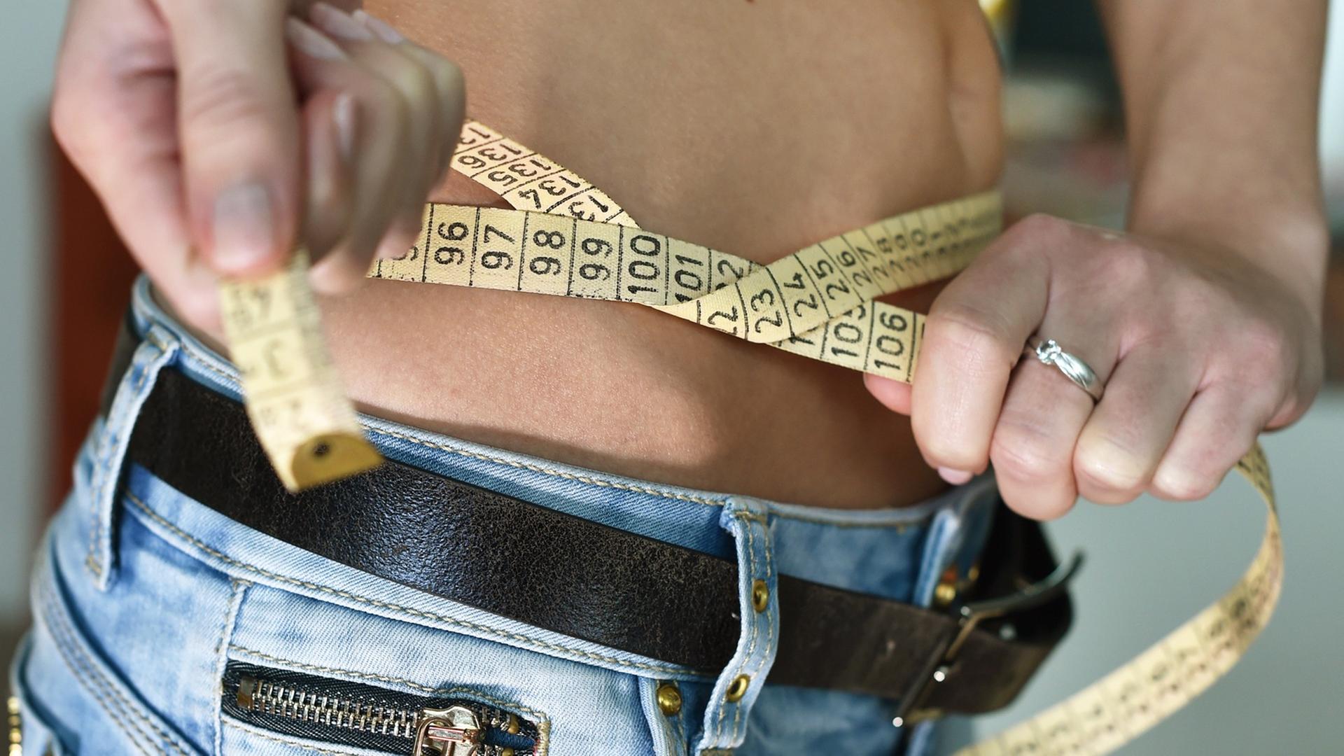 Eine junge Frau mit einem Zentimetermaß um den Bauch. Eine junge Frau mit einem Zentimetermaß um den Bauch.