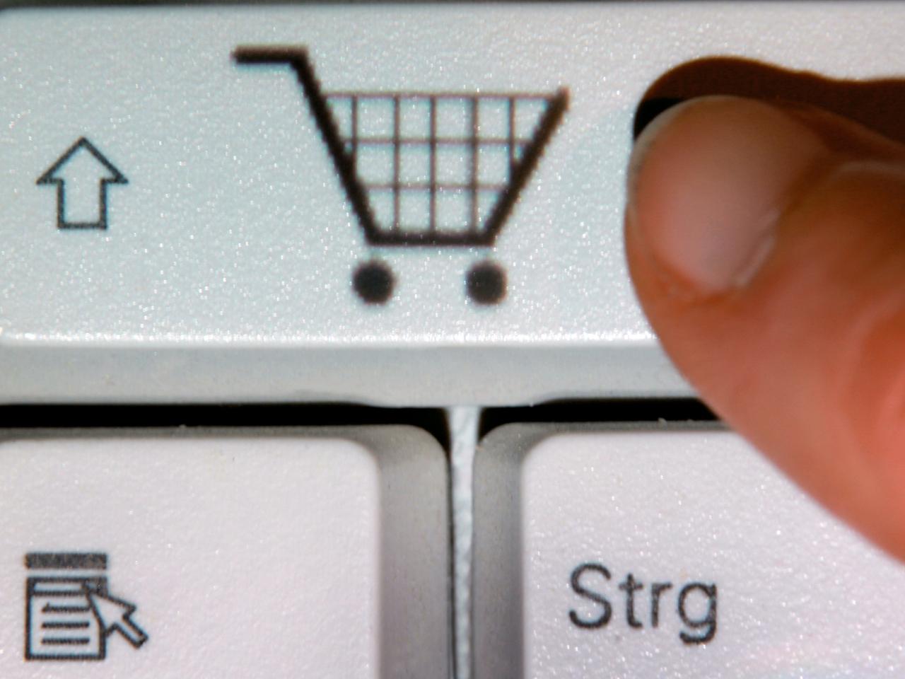 Ein Finger zeigt auf das Symbol eines Einkaufwagens auf einer Taste einer Computertastatur (gestelltes Foto). Ein Finger zeigt auf das Symbol eines Einkaufwagens auf einer Taste einer Computertastatur (gestelltes Foto).