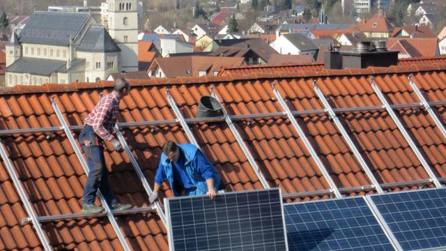 Arbeiter installieren Solarzellen auf einem Dach,
