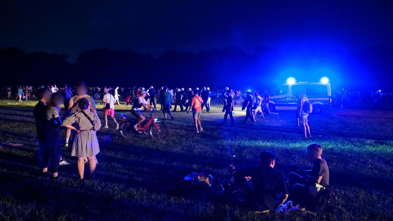 Behelmte Polizisten laufen in Hamburg begleitet von einem Mannschaftswagen mit Blaulicht durch die Menschengruppen auf der Stadtpark-Wiese. Behelmte Polizisten laufen in Hamburg begleitet von einem Mannschaftswagen mit Blaulicht durch die Menschengruppen auf der Stadtpark-Wiese.