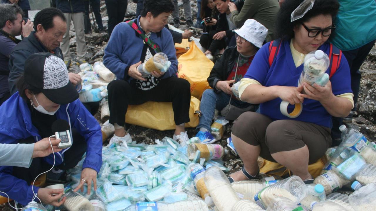 Gruppe Koreaner sitzt vor Plastikflaschen und befüllt sie. Gruppe Koreaner sitzt vor Plastikflaschen und befüllt sie.