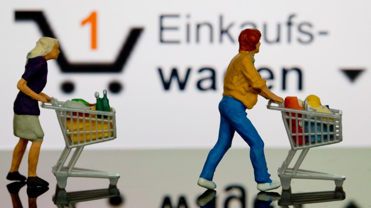 Zwei kleine Plastikfiguren mit Einkaufswagen stehen vor einem iPhone, auf dem der virtuelle Einkaufswagen dargestellt ist. Zwei kleine Plastikfiguren mit Einkaufswagen stehen vor einem iPhone, auf dem der virtuelle Einkaufswagen dargestellt ist.