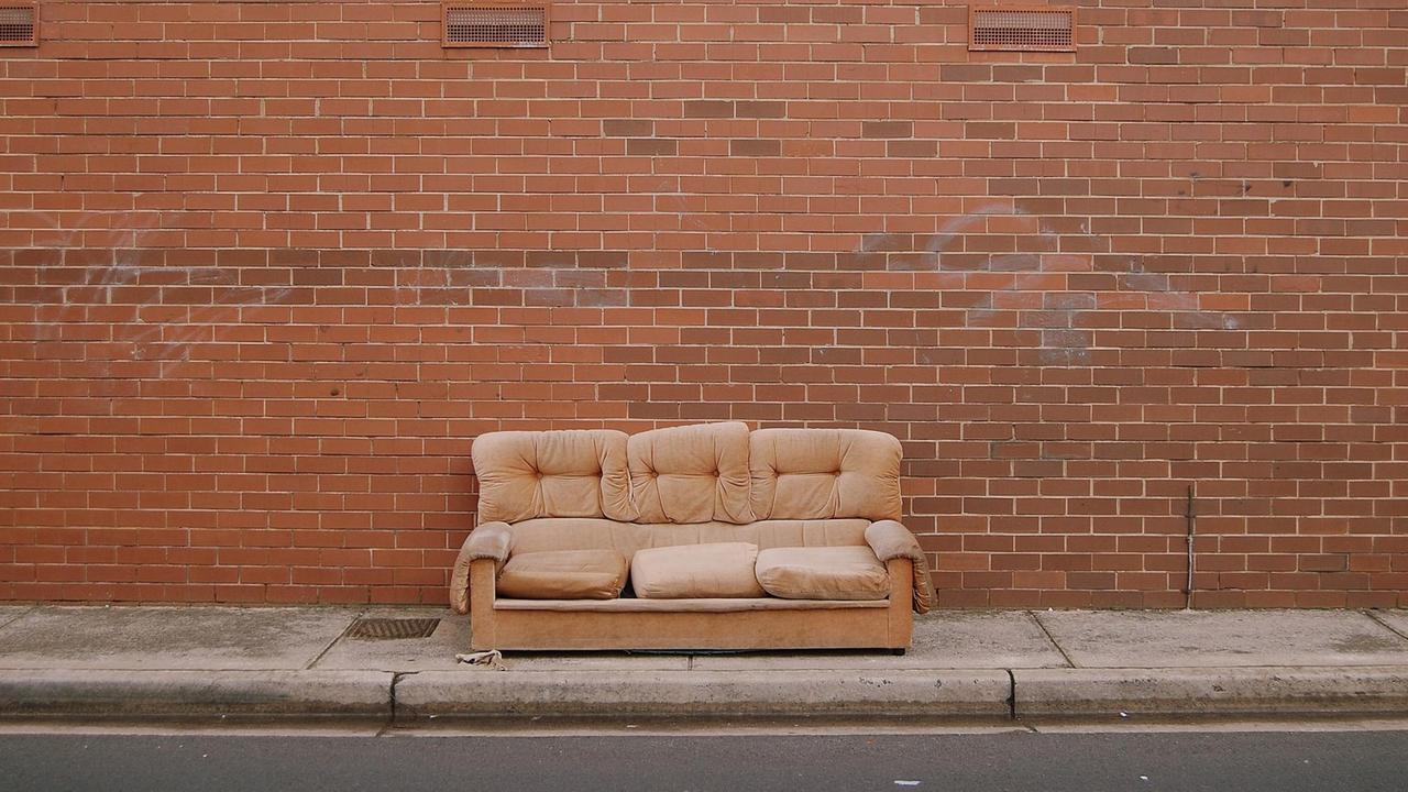 Ein altes, zerbeultes Sofa steht vor einer roten Backsteinmauer. Ein altes, zerbeultes Sofa steht vor einer roten Backsteinmauer.