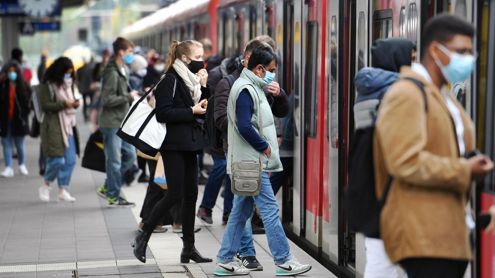 Auf einem Bahnsteig steigen Fahrgäste mit Mund-Nasen-Schutz in einen Zug.