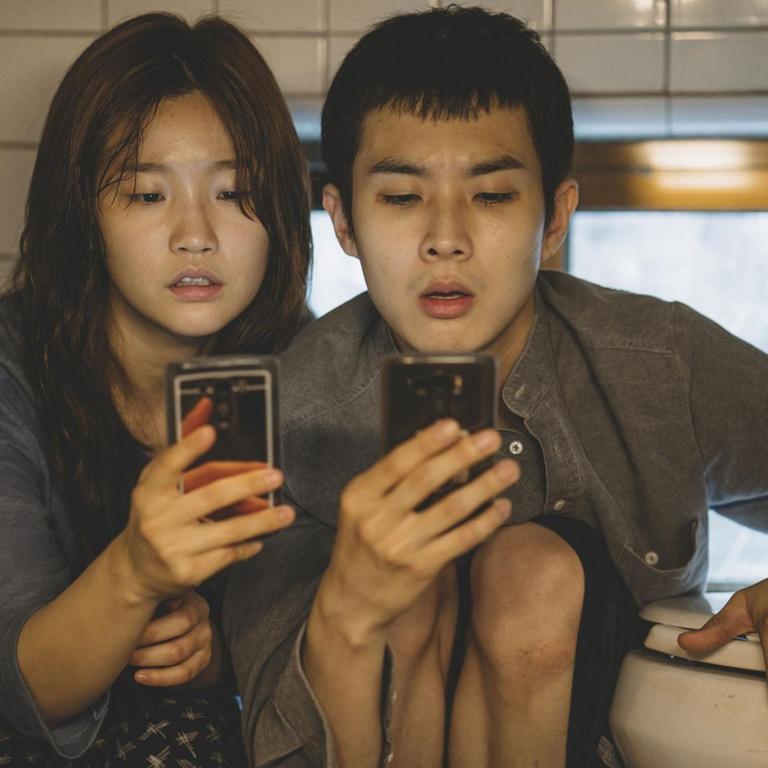 Szene aus dem Film "Parasite" von Regisseur Joon-ho Bong. Eine junge Frau und ein junger Mann sitzen in einem Badezimmer und starren auf ihr Smartphone.