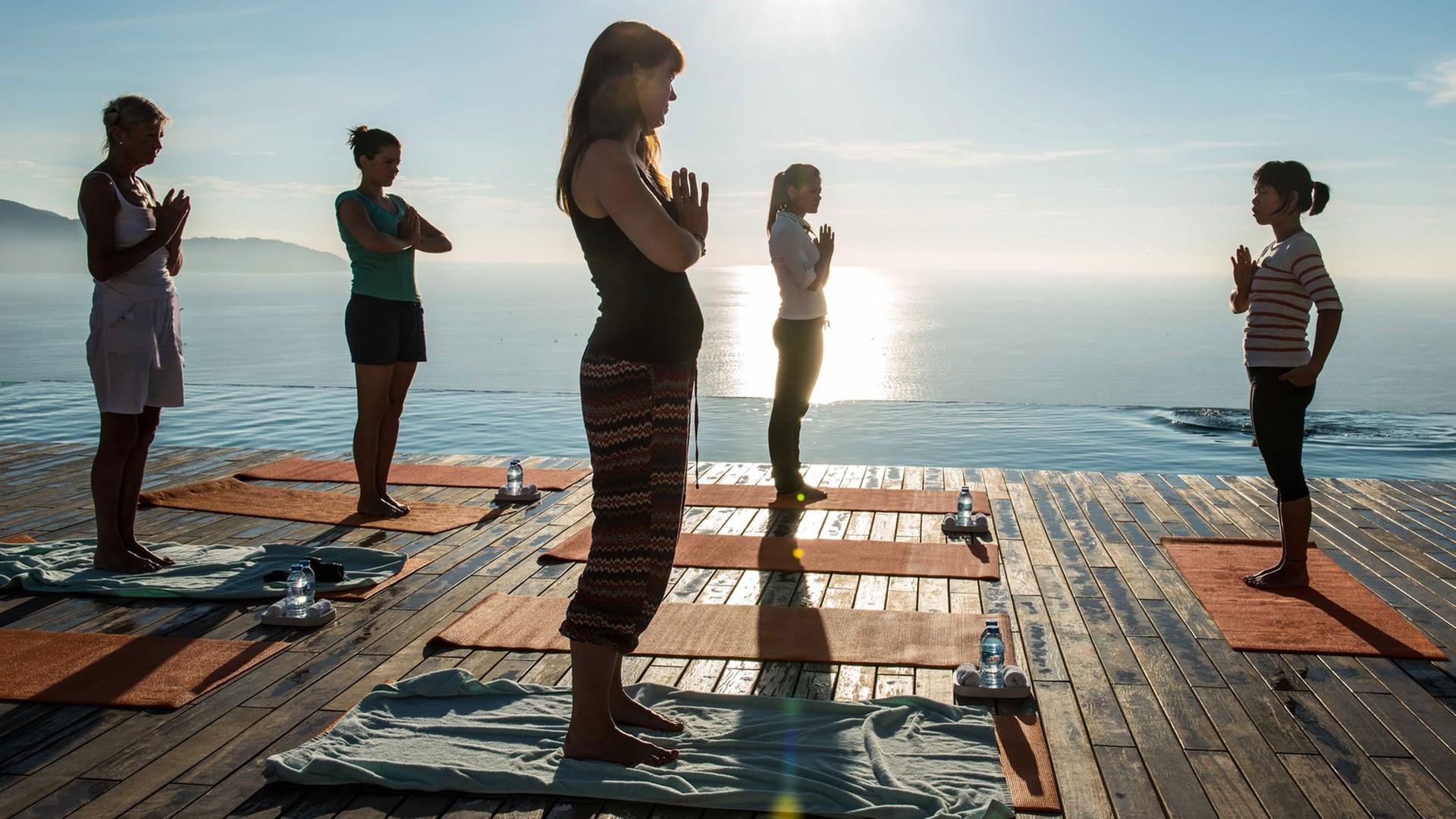Menschen machen in der Morgensonne Yoga-Übungen am Meer.