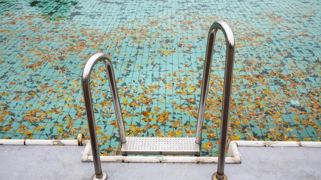 Ein verlassenes Schwimmbecken mit Laub zum Saisonende im Herbst