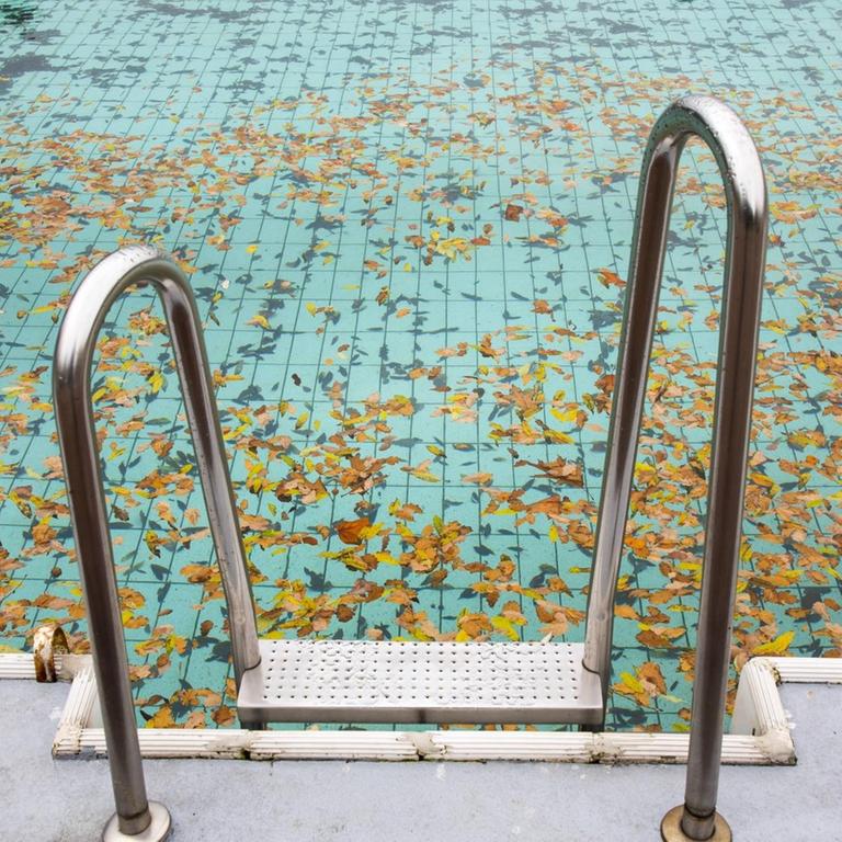 Ein verlassenes Schwimmbecken mit Laub zum Saisonende im Herbst
