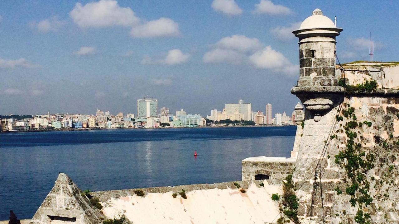 Von einem hohen Steingebäude mit kleinen Zinnen aus sieht man über einen Fluss auf die Skyline von Havanna in der Ferne.