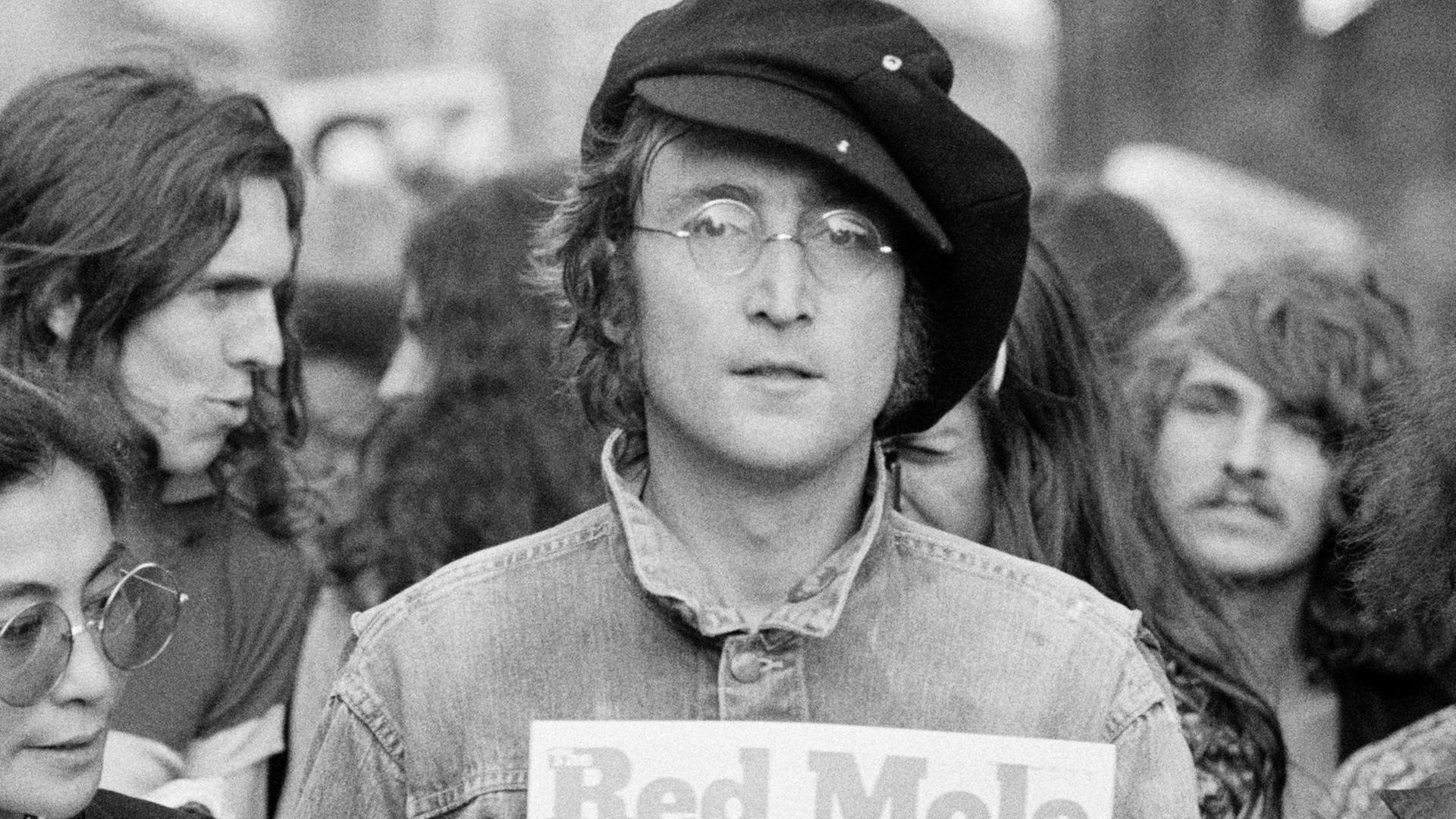 Schwarzweiß Fotografie von John Lennon im Hyde Park. Neben ihm steht Yoko Ono, im Hintergrund stehen weitere junge Menschen.