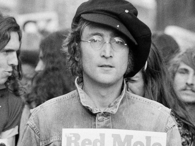 Schwarzweiß Fotografie von John Lennon im Hyde Park. Neben ihm steht Yoko Ono, im Hintergrund stehen weitere junge Menschen.