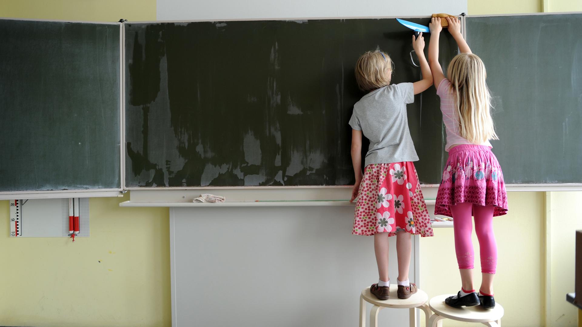 Zwei Grundschülerinnen wischen die Tafel blank. Zwei Grundschülerinnen wischen die Tafel blank.