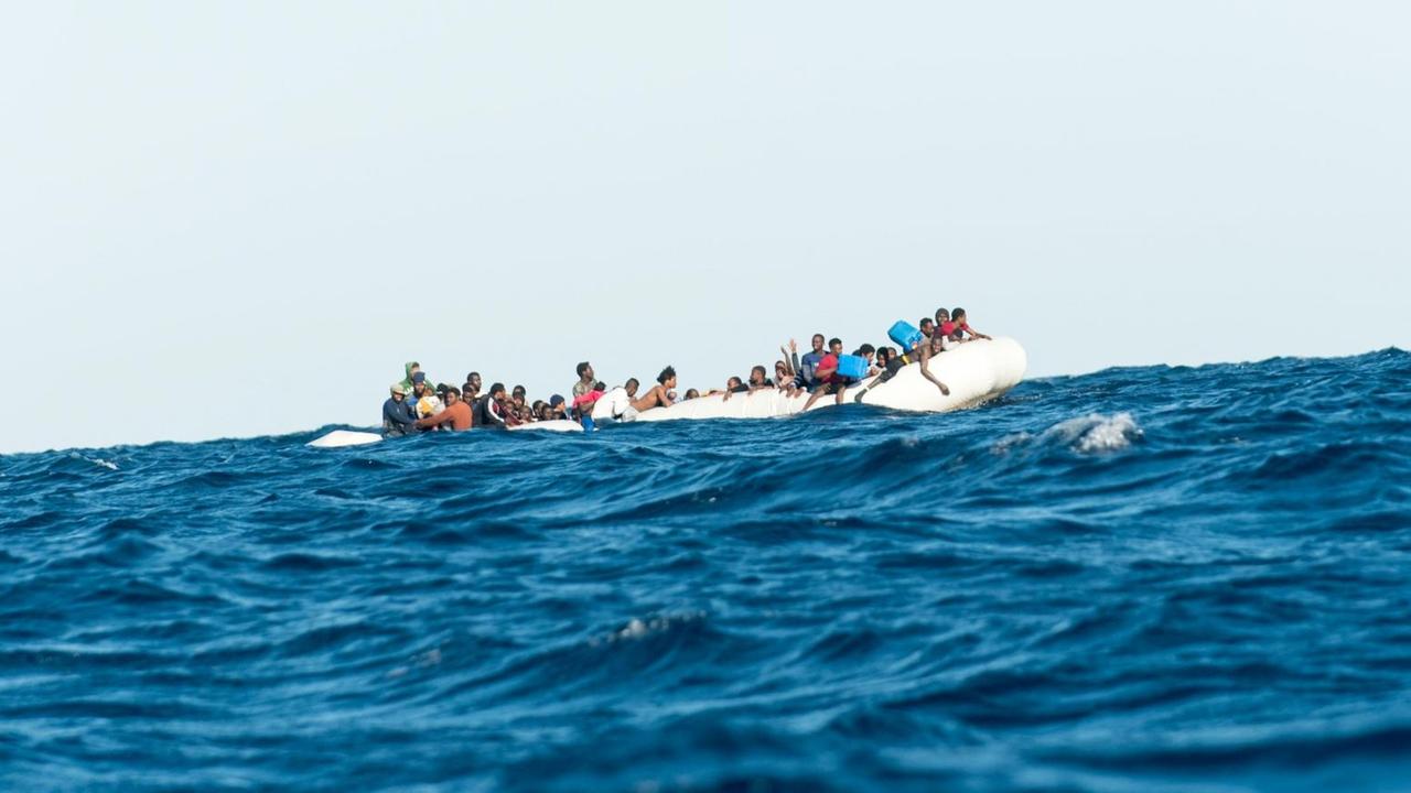 Migranten, die von Libyen aus nach Italien wollen, sitzen auf einem Schlauchboot im Mittelmeer.