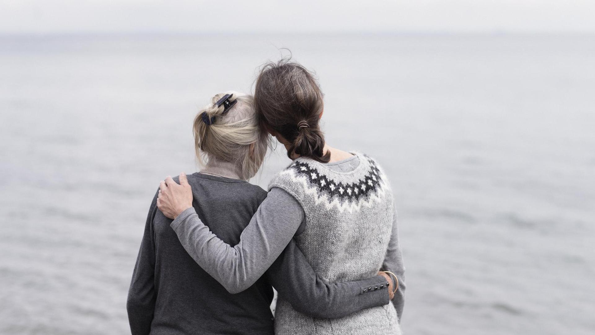 Zwei erwachsene Frauen, Mutter und Tochter stehen Arm in Arm am Meer. Zwei erwachsene Frauen, Mutter und Tochter stehen Arm in Arm am Meer.