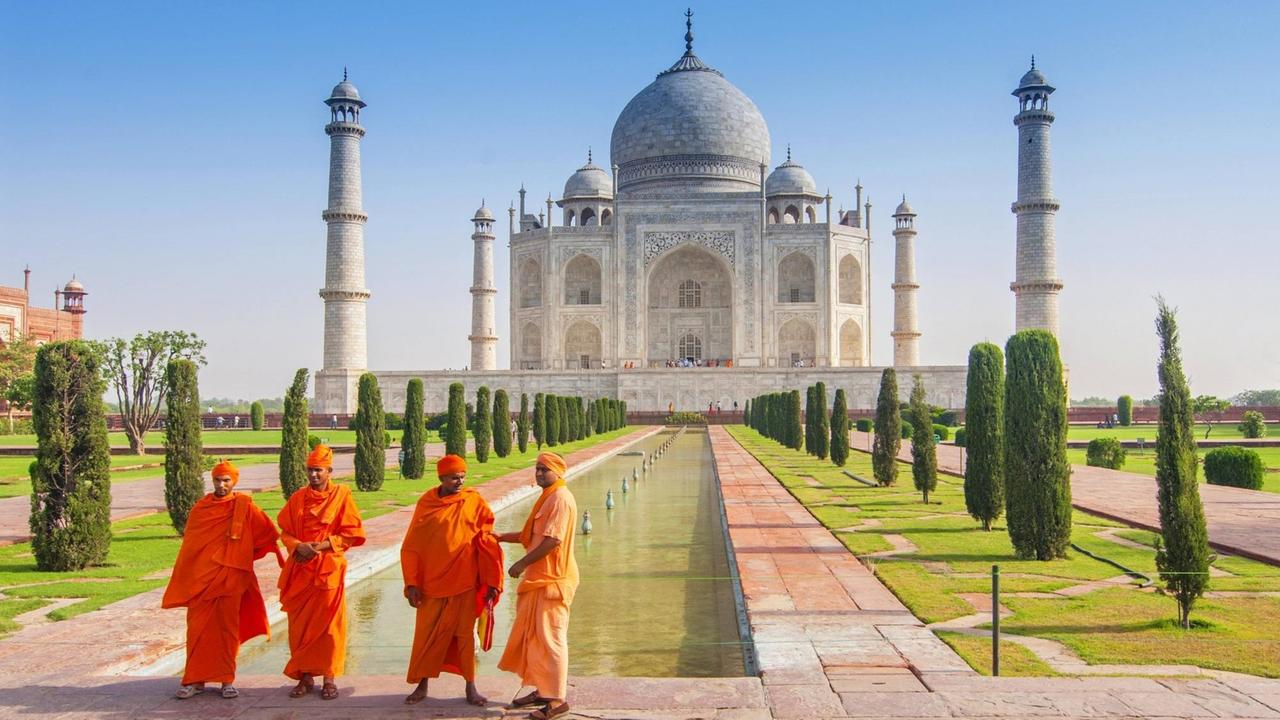 Pilger in orangenen Kutten im der Gartenanlage des Taj Mahal.