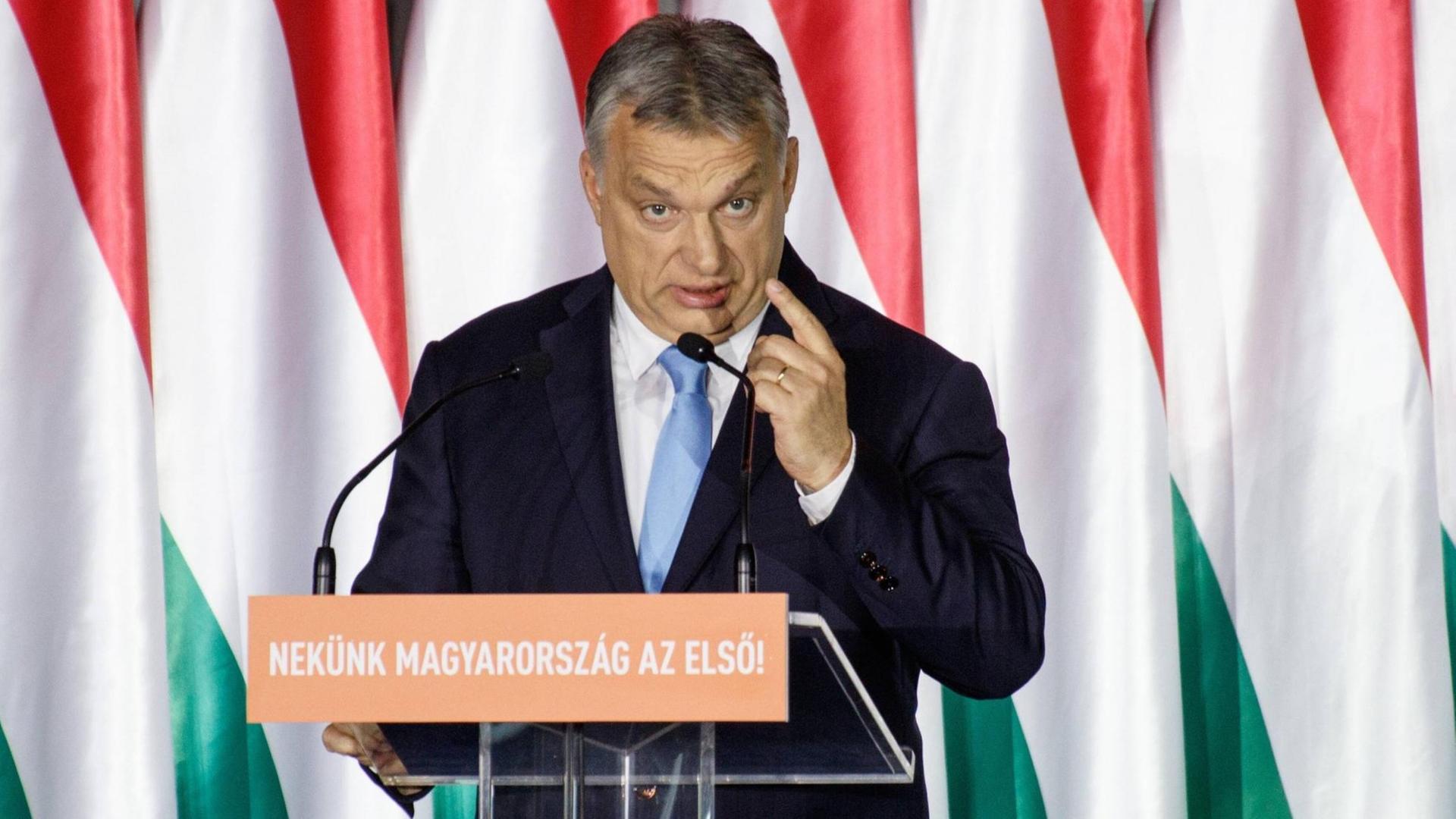 Ungarns Ministerpräsident Viktor Orbán steht bei einer Rede an einem Pult und hebt die linke Hand Ungarns Ministerpräsident Viktor Orbán steht bei einer Rede an einem Pult und hebt die linke Hand