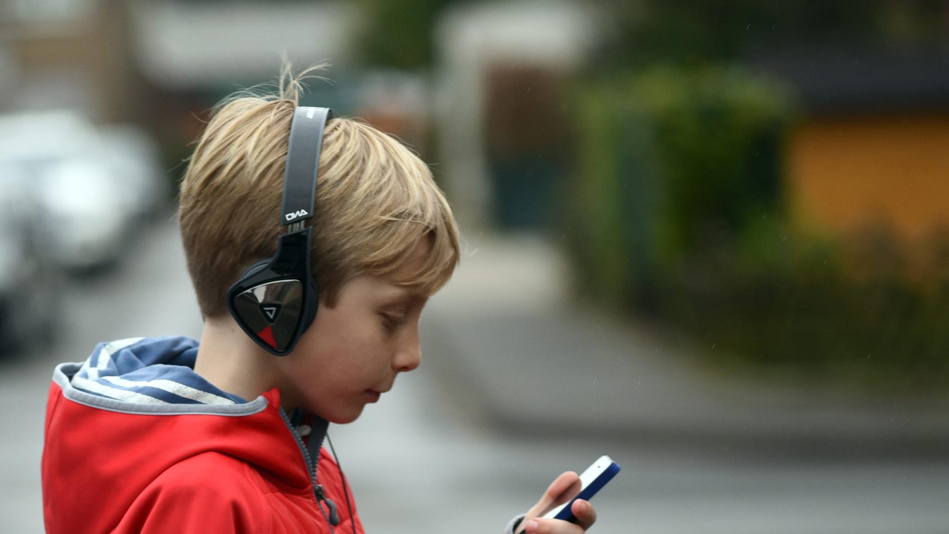 Ein Junge spaziert mit Kopfhörern und iPhone. Ein Junge spaziert mit Kopfhörern und iPhone.