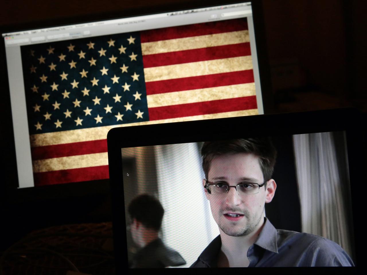 Edward Snowden auf einem Bildschirm vor einer US-Flagge Edward Snowden auf einem Bildschirm vor einer US-Flagge