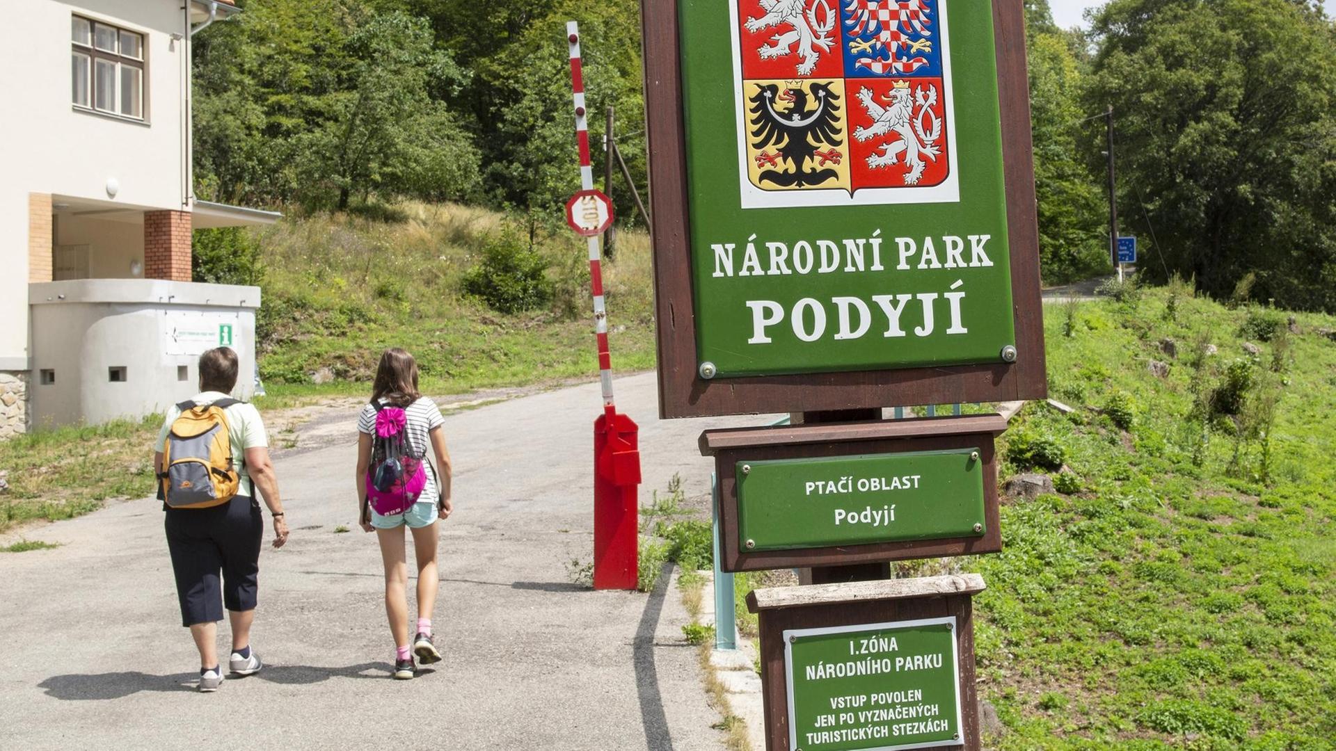 Zwei Kinder mit Rucksäcken laufen auf eine rot-weiße Schranke am Eingang des Thayatal-Nationalparks in Tschechien zu. Zwei Kinder mit Rucksäcken laufen auf eine rot-weiße Schranke am Eingang des Thayatal-Nationalparks in Tschechien zu.