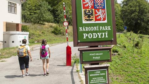 Zwei Kinder mit Rucksäcken laufen auf eine rot-weiße Schranke am Eingang des Thayatal-Nationalparks in Tschechien zu.