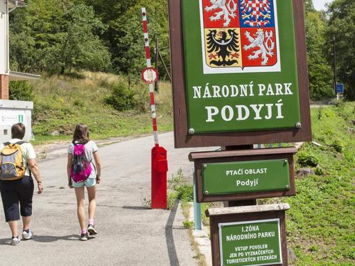 Zwei Kinder mit Rucksäcken laufen auf eine rot-weiße Schranke am Eingang des Thayatal-Nationalparks in Tschechien zu.