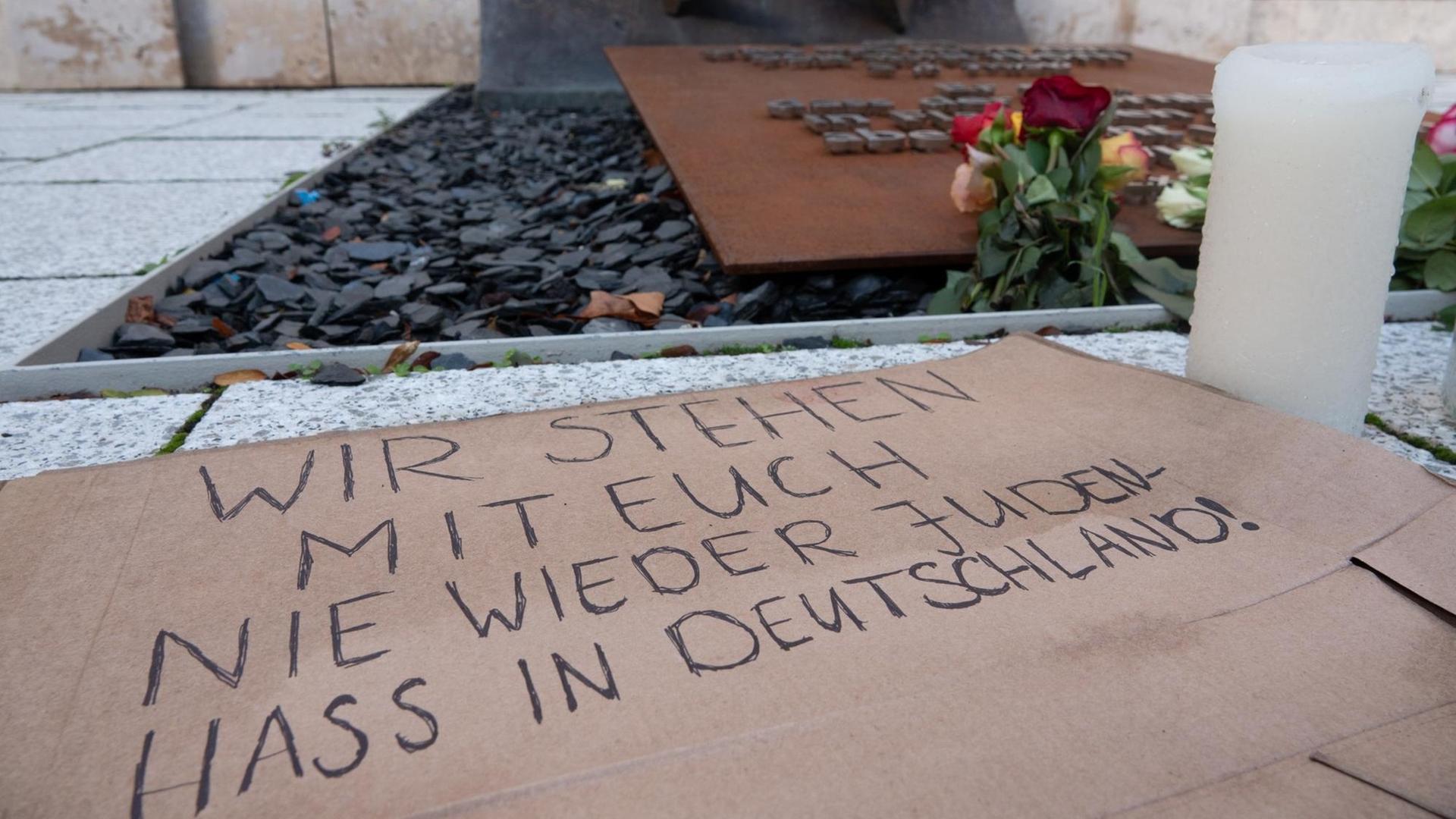 Ein Pappkarton mit der Aufschrift «Wir stehen mit euch nie wieder Judenhass in Deutschland!», Blumen und Kerzen sind vor einer Synagoge abgelegt.