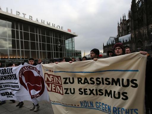 Demonstranten mit Transparenten vor dem Hauptbahnhof, darauf zu lesen "Nein zu Rassismus, nein zu Sexismus".