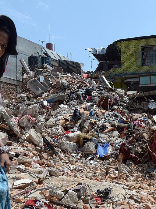 Eine Frau in Nepal läuft an einem zerstörten Haus vorbei.