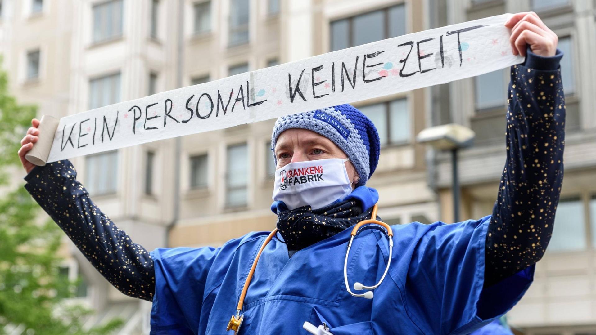 Eine Pflegekraft mit Mundschutz hält ein Banner in die Luft, auf dem Zeit- und Personalmangel beklagt wird. Eine Pflegekraft mit Mundschutz hält ein Banner in die Luft, auf dem Zeit- und Personalmangel beklagt wird.