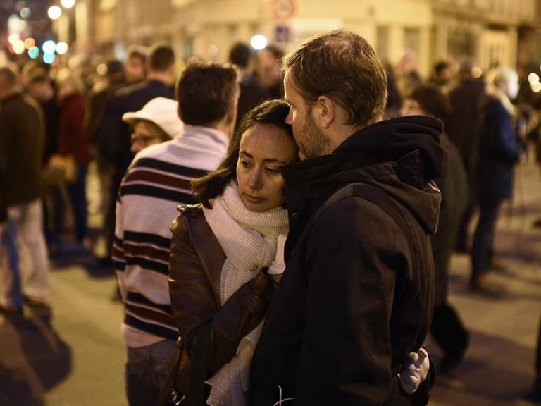 Ein Paar steht am Abend engumschlungen auf der Straße. Um sie herum stehen viele weitere Menschen.