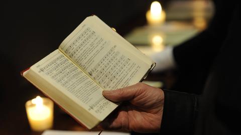 Mann mit einem Gesangsbuch in der Hand, umrahmt von zwei Kerzen