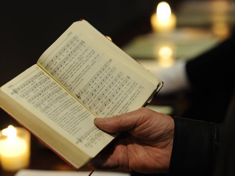 Mann mit einem Gesangsbuch in der Hand, umrahmt von zwei Kerzen