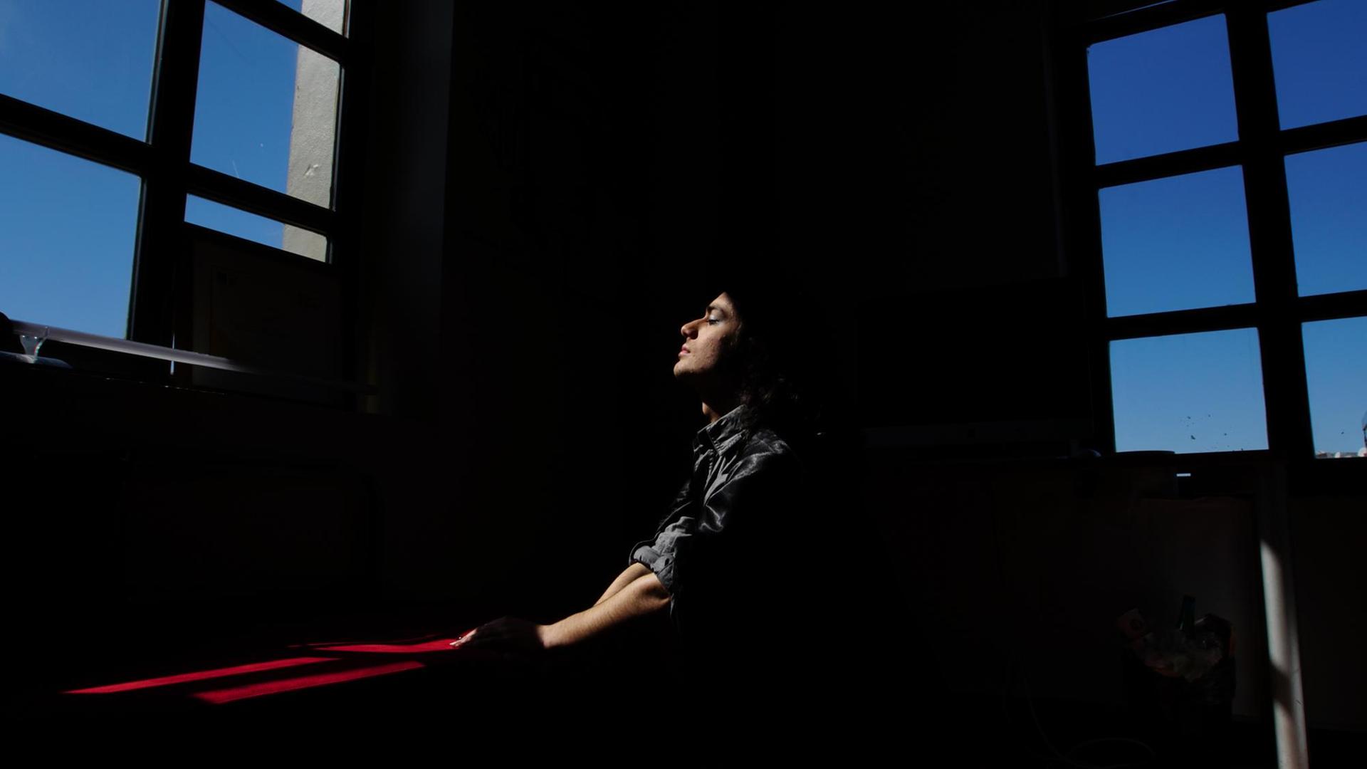 Eine Person sitzt meditierend vor einem Fenster. Eine Person sitzt meditierend vor einem Fenster.
